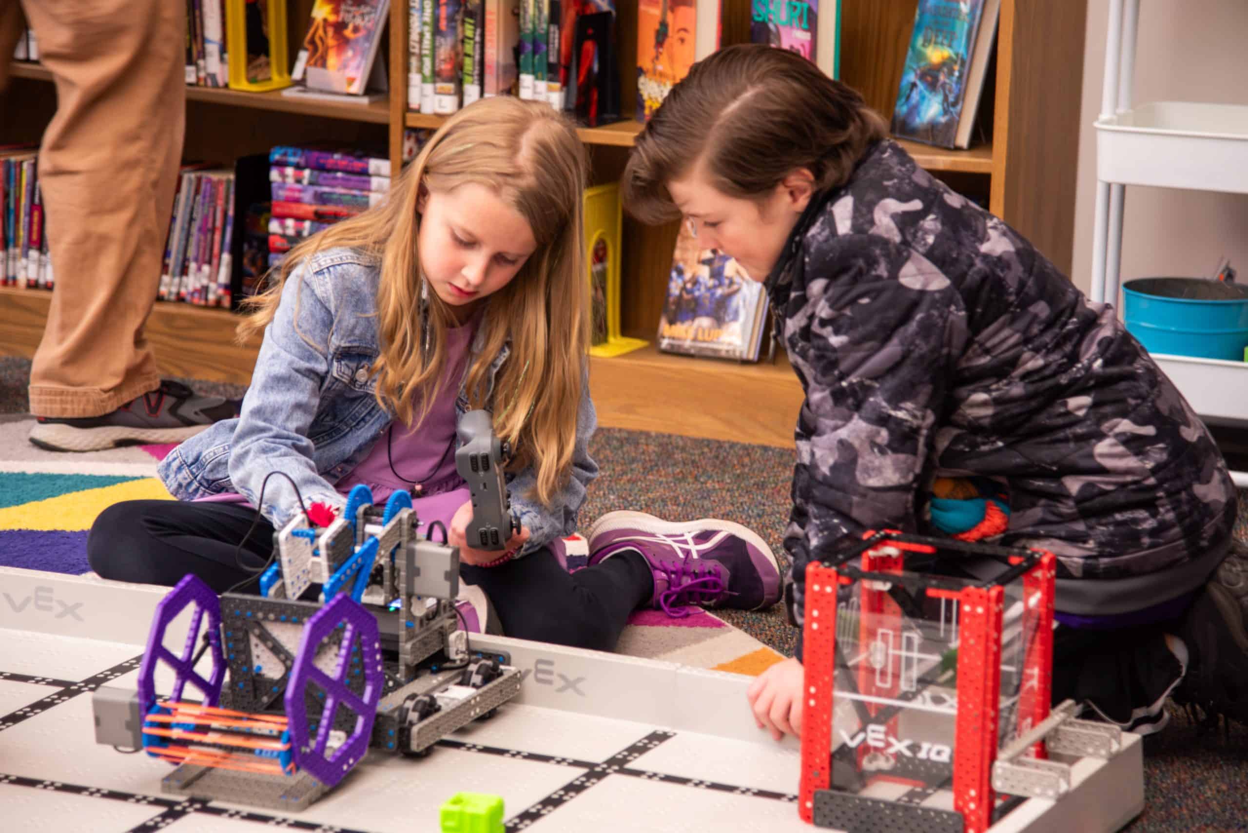Students examine a VEX robot on a field